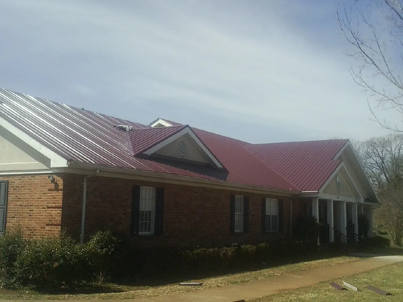 Red metal roof with gabled entries on a long brick building, from a Hail Damage Roof Repair job in Falls Church