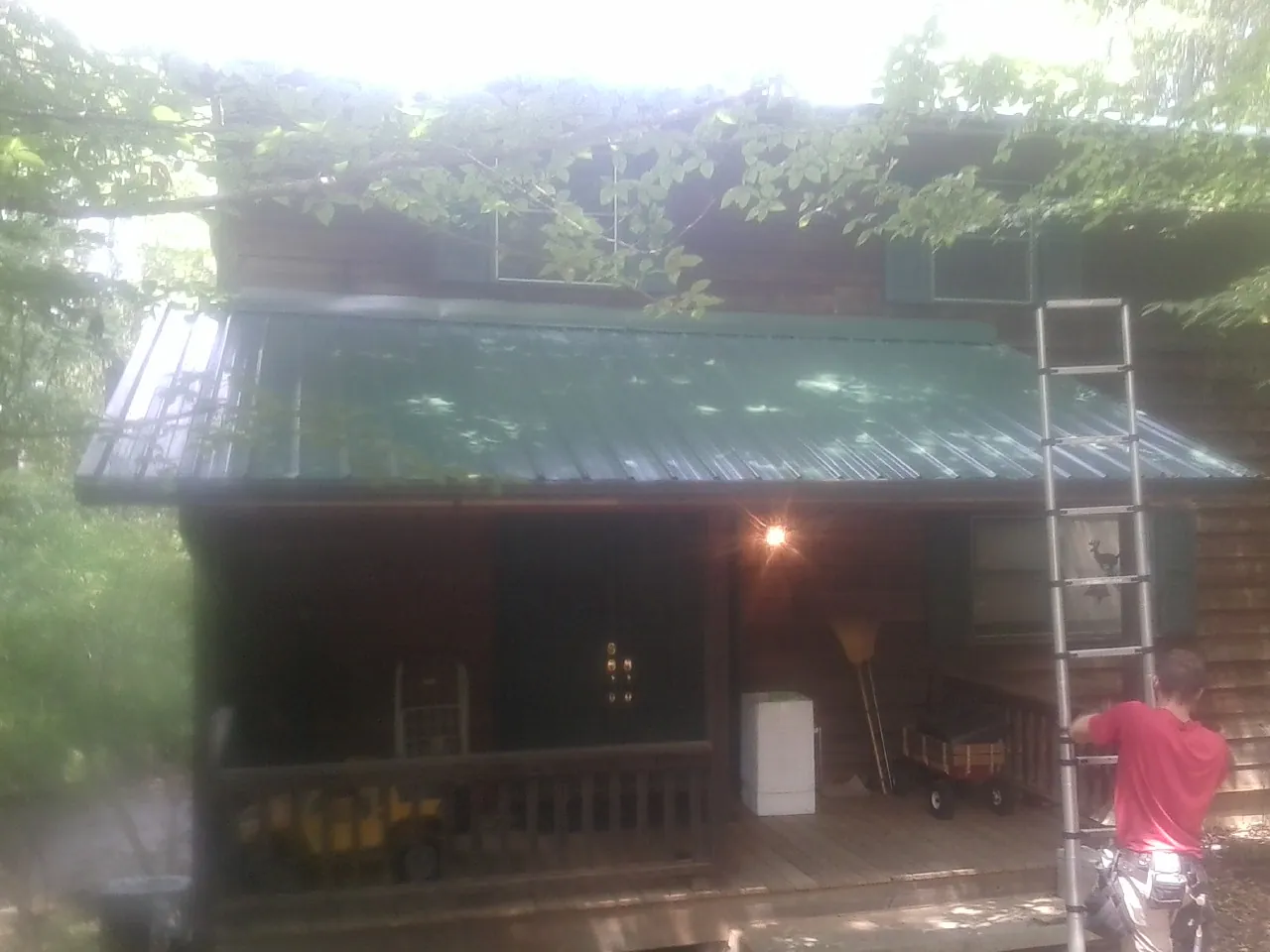 Worker on a ladder at the green porch roof of a wooded cabin in Falls Church