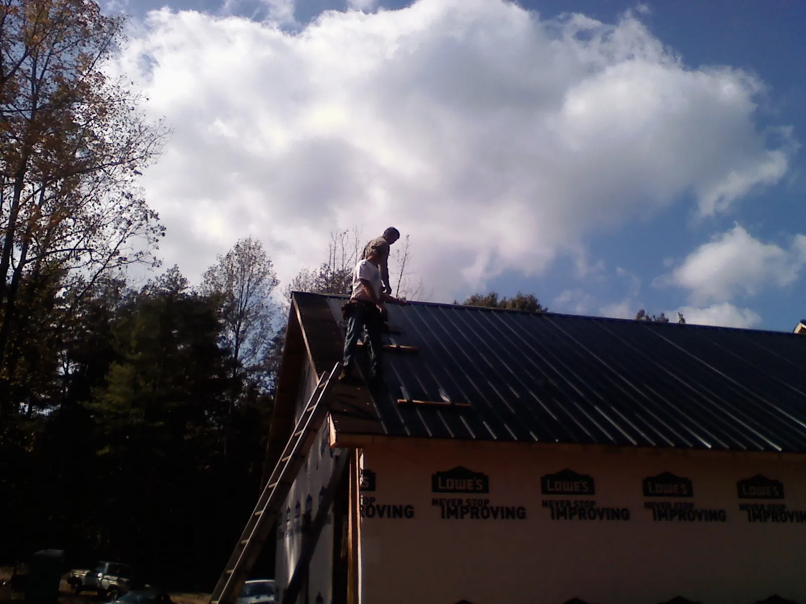 Roofer fastening dark metal panels high against a cloudy sky, from a Roof Inspection job in Falls Church