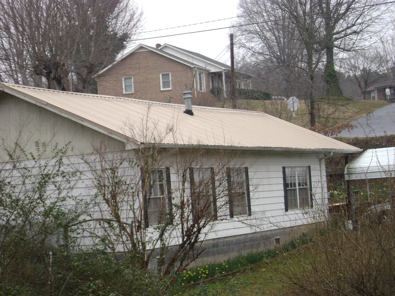Tan metal roof on a white sided house set into a hillside — Commercial Roofing by Roofing Brothers in Falls Church